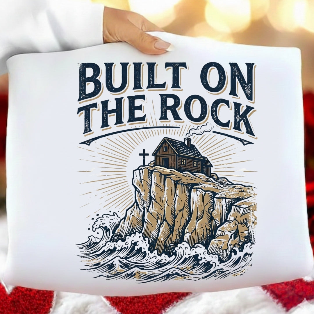 White pillow with 'Built on the Rock' text and rock illustration held by a person.
