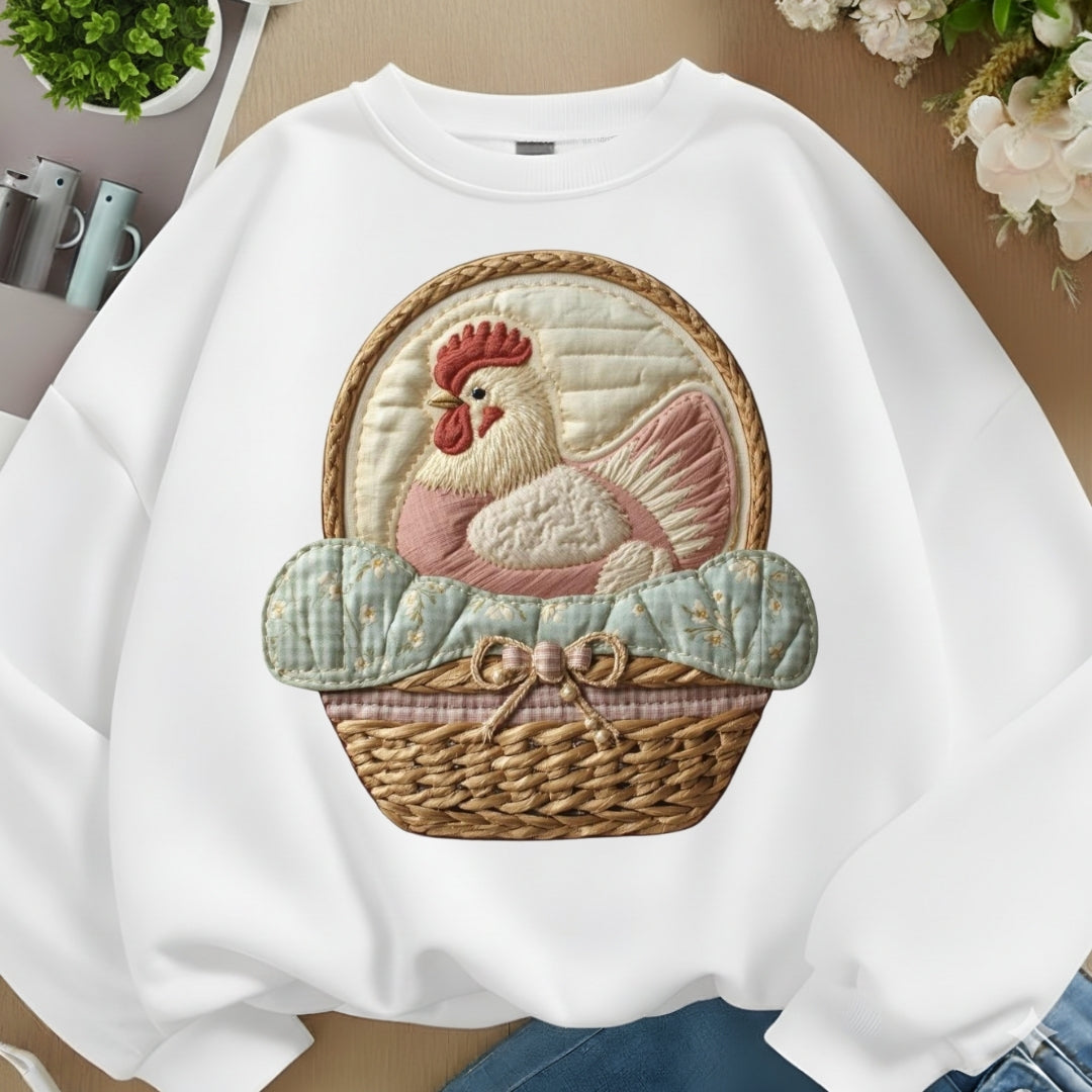 White sweatshirt with a rooster design in a basket on a neutral background