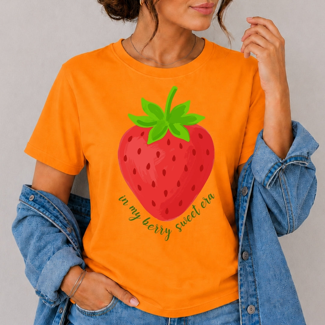 Person wearing an orange t-shirt with a strawberry graphic and text.