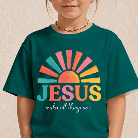 A child wearing a dark teal t-shirt with a colorful retro sunburst graphic and the text 'JESUS makes all things new' printed on the front, set against a textured beige wall.