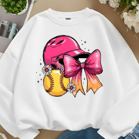 A white crewneck sweatshirt featuring a colorful graphic of a pink softball helmet, a yellow softball, and a pink-to-orange bow, styled in a flat-lay arrangement with flowers and plants.