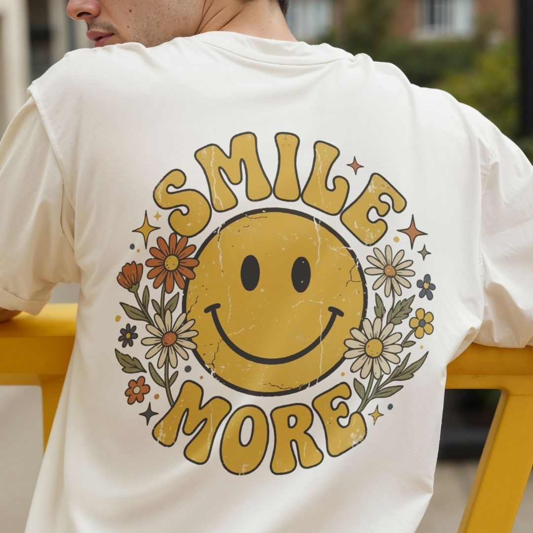 Close up of the back of a man's cream t-shirt showing a large distressed style yellow smiley face design with floral details and groovy lettering.