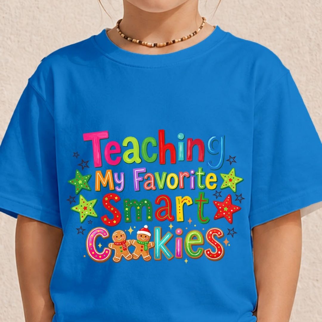 A bright blue short-sleeve t-shirt with a colorful graphic text reading 'Teaching My Favorite Smart Cookies' in multicolored letters with stars and gingerbread cookies, worn by a model.