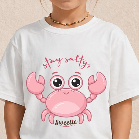 A young person wearing a white t-shirt featuring a large cartoon pink crab graphic and the text "stay salty, Sweetie".