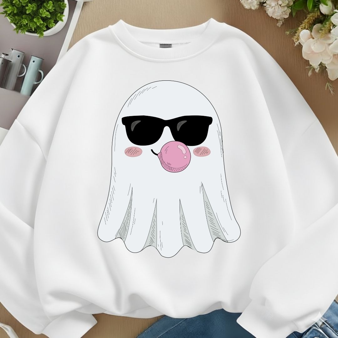 A white crewneck sweatshirt featuring a cartoon ghost graphic wearing black sunglasses and blowing a pink bubblegum bubble, displayed on a wooden surface with lifestyle props.