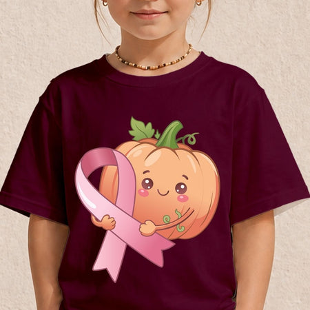 A child wearing a dark maroon short-sleeve t-shirt with a cute graphic of a smiling orange pumpkin hugging a pink breast cancer ribbon.
