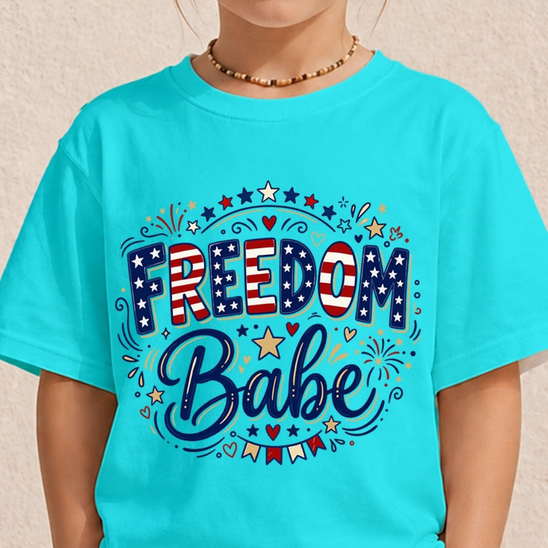A close-up of a person wearing a bright turquoise short-sleeve graphic T-shirt. The shirt features a patriotic design with the words 'FREEDOM Babe' in red, white, and blue lettering, decorated with stars, hearts, and small flag banners.