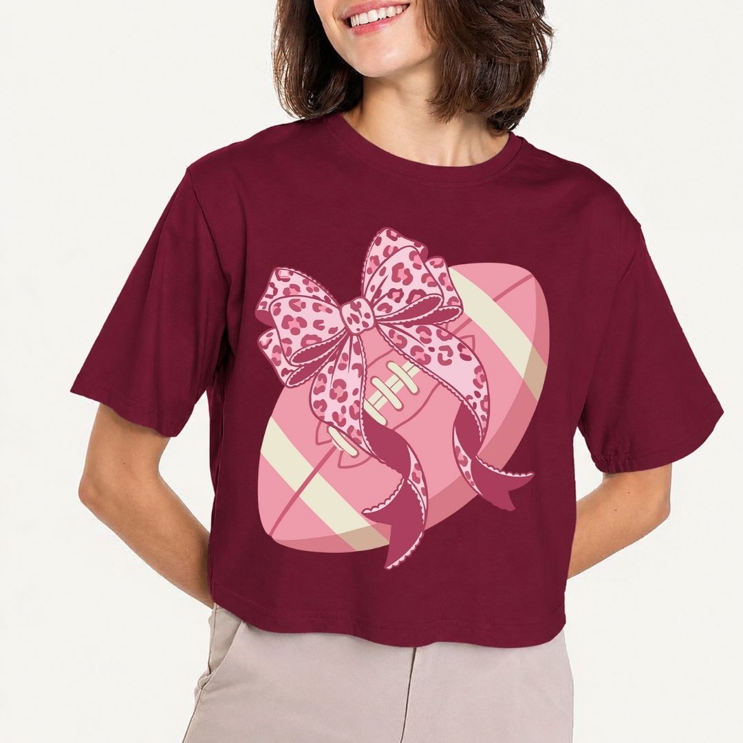 Person wearing a maroon t-shirt with a pink bow and football design on a plain background