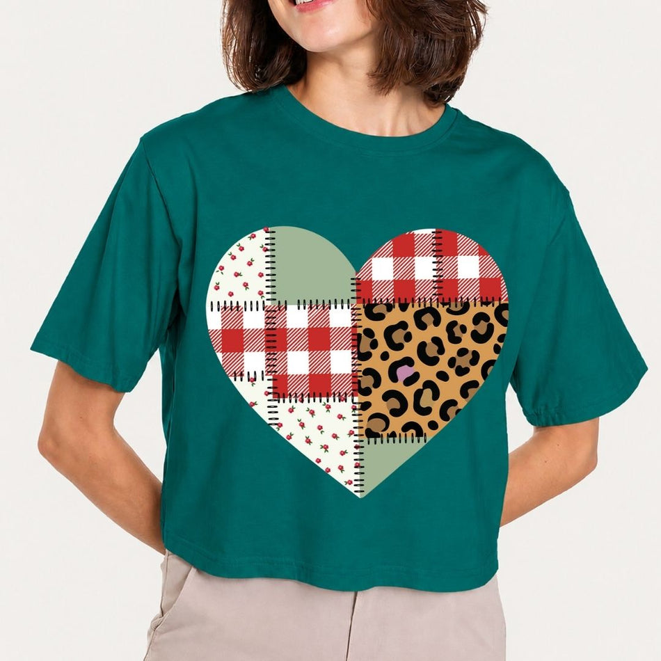 Person wearing a teal t-shirt with a heart-shaped patchwork design on a plain background