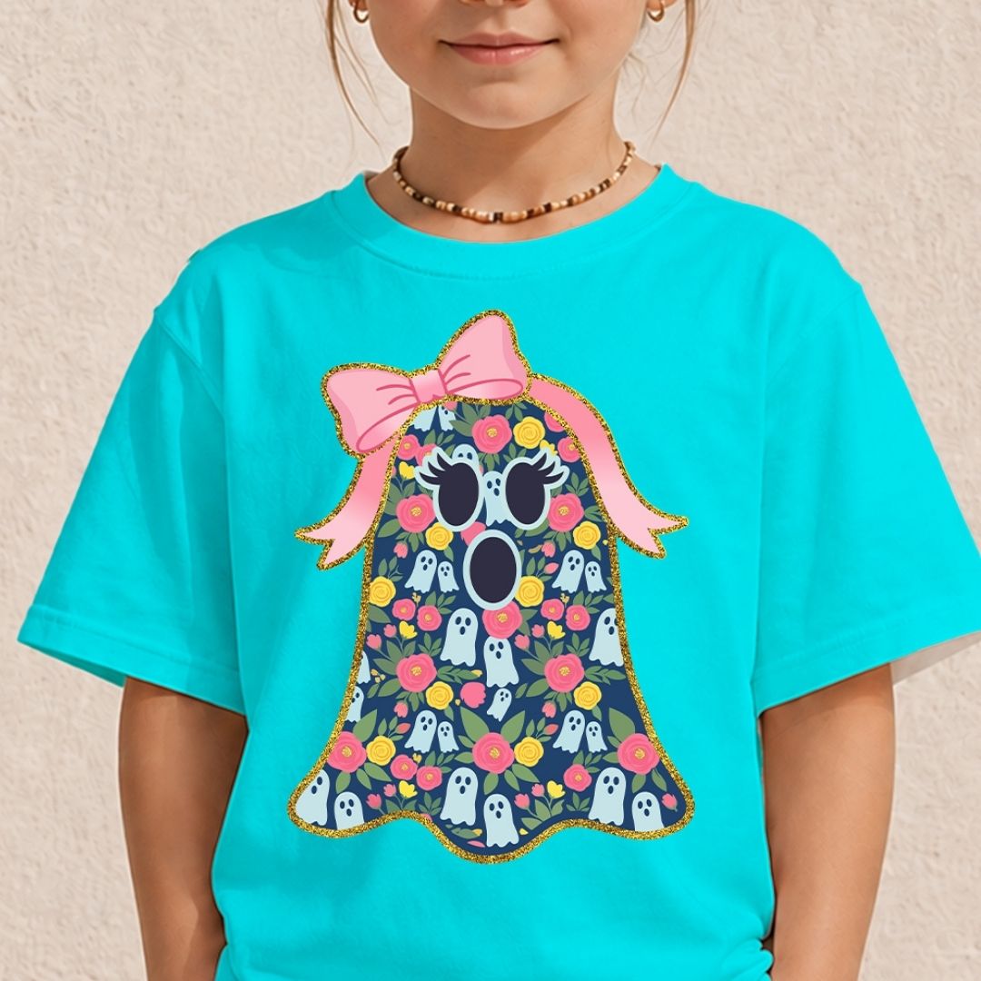 A child wearing a bright turquoise short-sleeve T-shirt with a large graphic of a ghost-shaped floral pattern topped with a pink bow, photographed against a light textured wall.