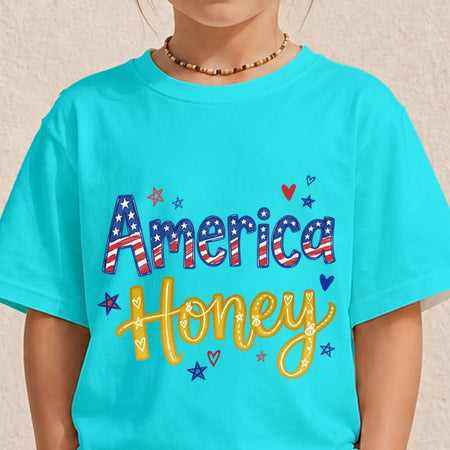 A child wearing a bright turquoise short-sleeve T-shirt with a patriotic graphic that reads 'America Honey' in red, white, and blue lettering with stars and hearts, against a light textured wall.