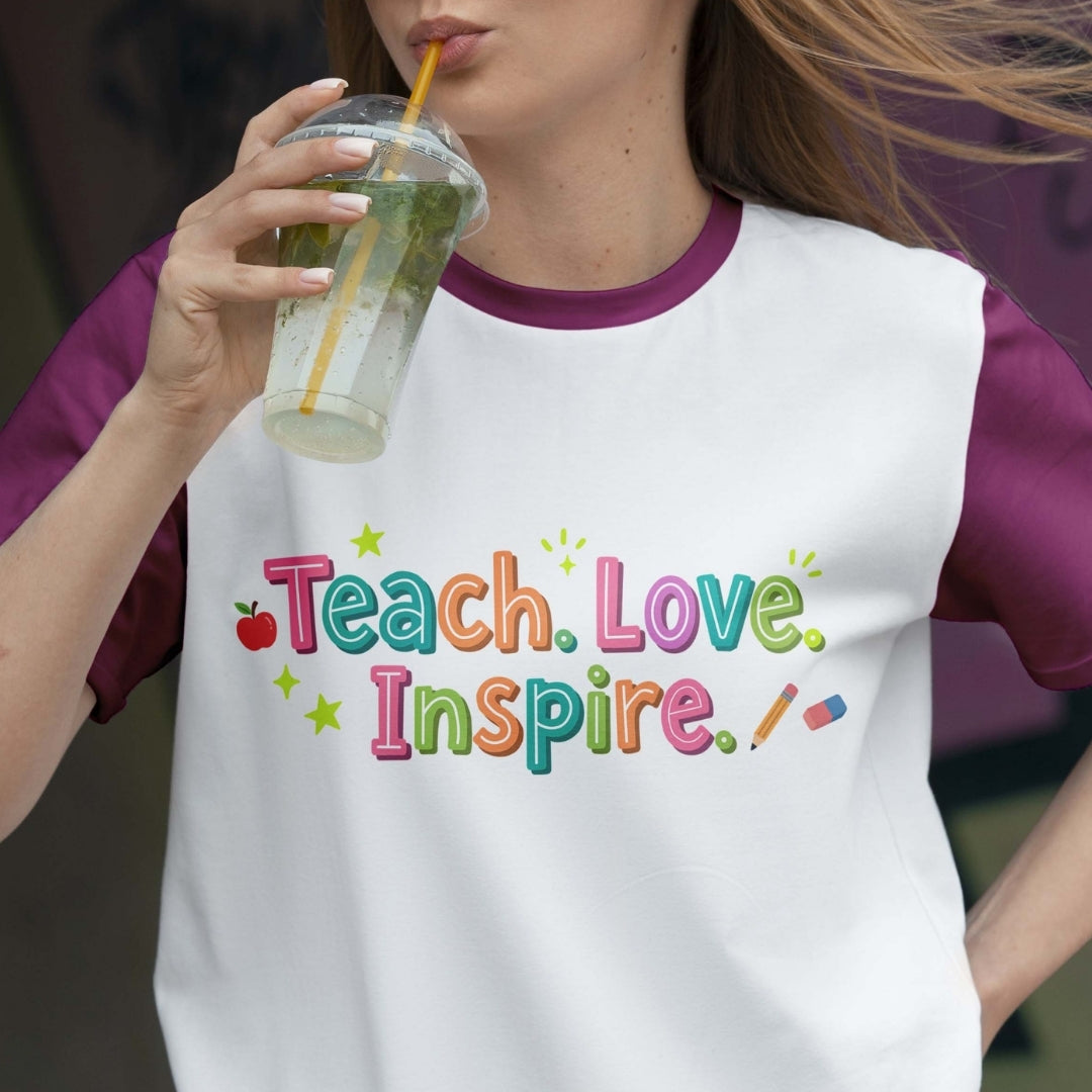 Person wearing a shirt with 'Teach. Love. Inspire.' text, holding a drink.