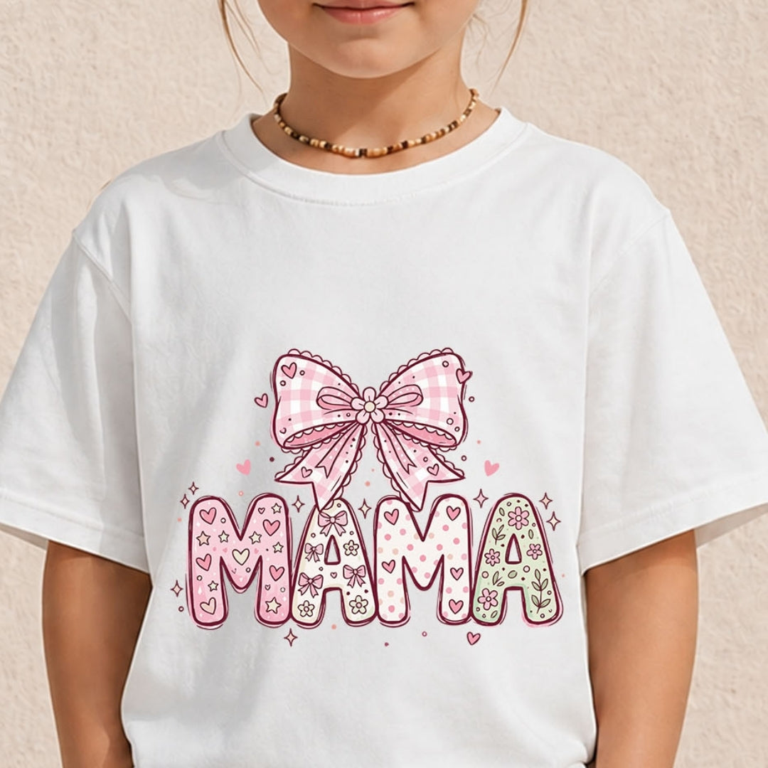 Close-up of a child wearing a white crewneck t-shirt printed with a decorative pastel pink "MAMA" letter design and patterned ribbon bow.