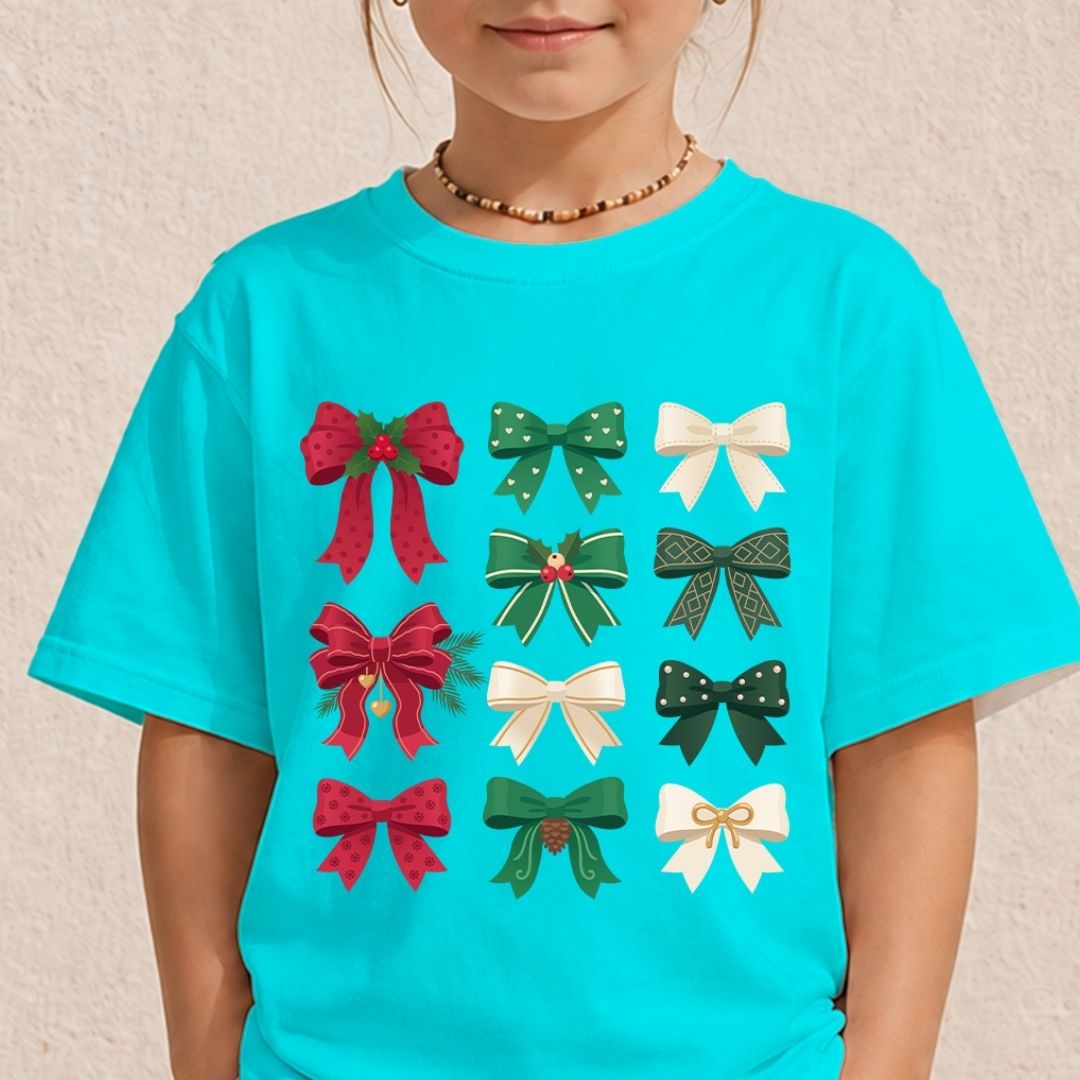 A child wearing a bright turquoise short-sleeve T-shirt with a graphic print of twelve festive ribbon bows in red, green, and white, set against a light beige textured wall.