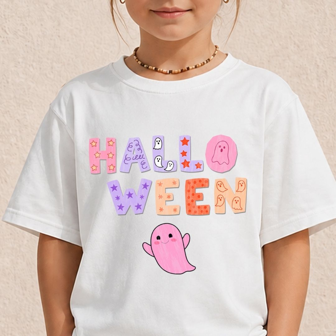 A child wearing a white short-sleeve T-shirt with a colorful 'HALLOWEEN' graphic and a pink ghost illustration on the front, photographed against a light beige textured wall.