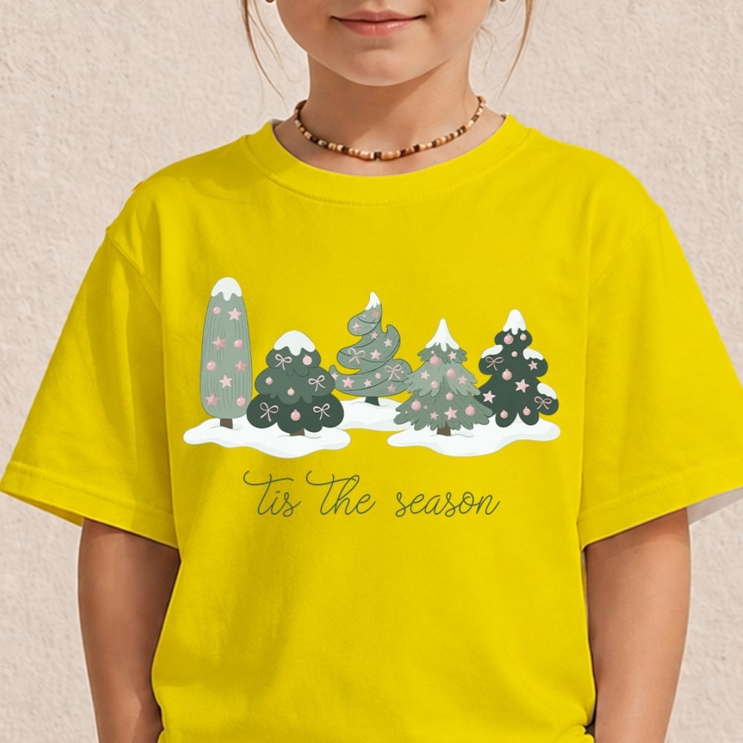 A child wearing a bright yellow t-shirt with a winter holiday graphic of snow-covered Christmas trees and the text 'Tis the season' printed on the front.