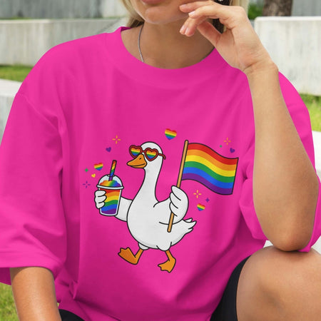 Person wearing a pink t-shirt with a colorful goose graphic holding a rainbow flag.