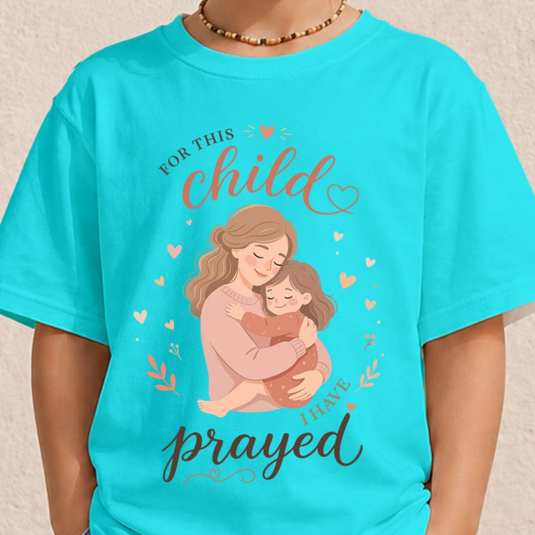 A person wearing a bright turquoise t-shirt featuring a mother-and-child illustration and the text "For this child I have prayed."