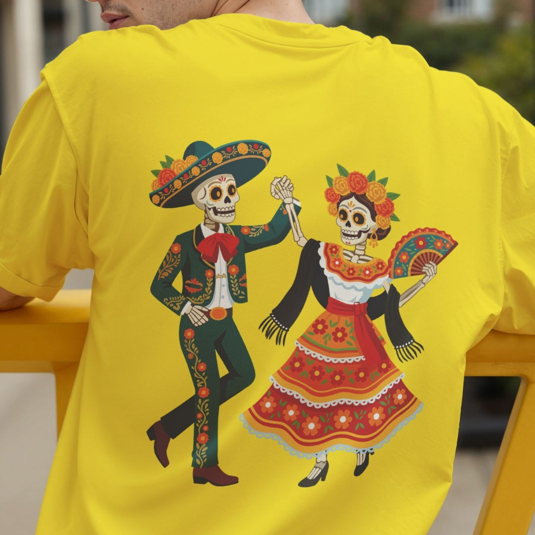 A person wearing a bright yellow T-shirt from the back, featuring a large colorful graphic of a dancing skeleton couple dressed in Day of the Dead attire.