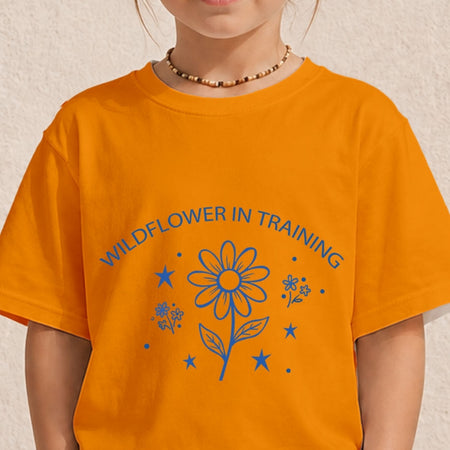Close-up of a child wearing a bright orange t-shirt printed with a blue minimal floral "Wildflower in Training" design.