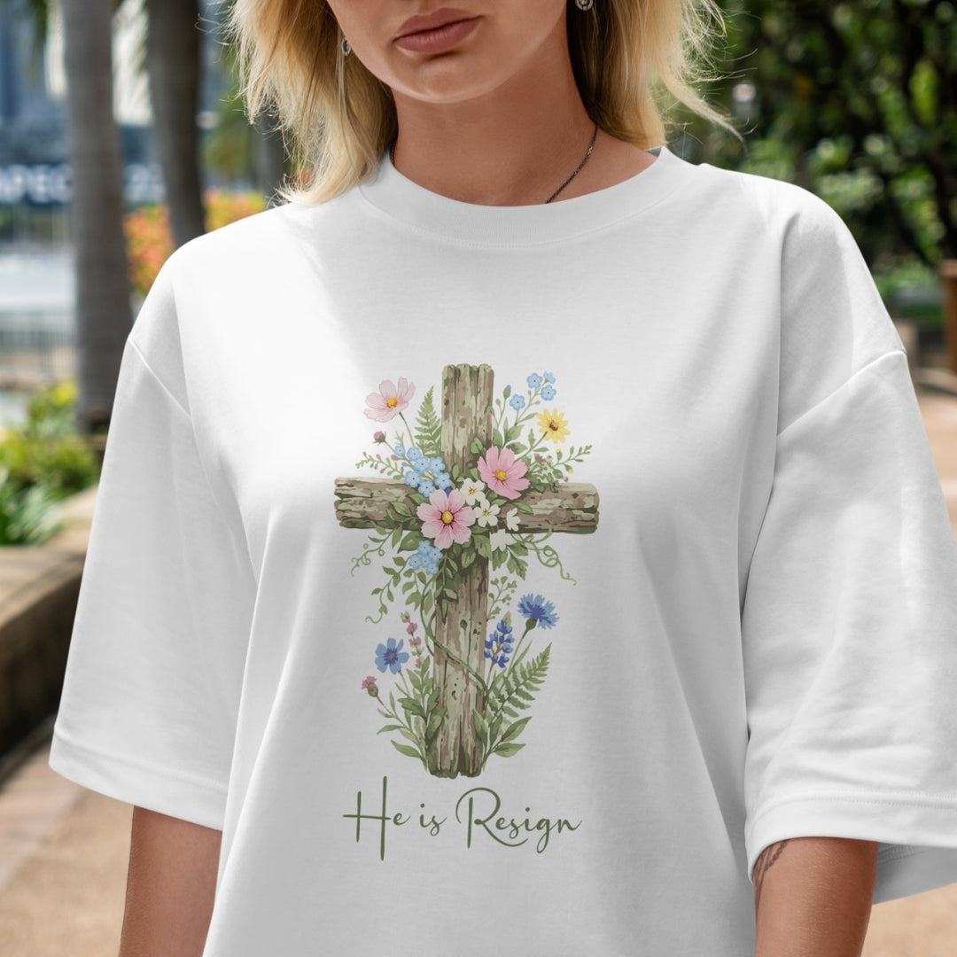 Person wearing a white t-shirt with a floral cross design and 'He is Risen' text.
