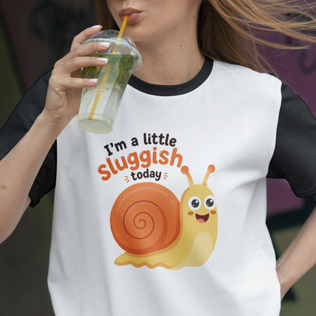 Person wearing a t-shirt with a snail graphic and text, holding a drink.