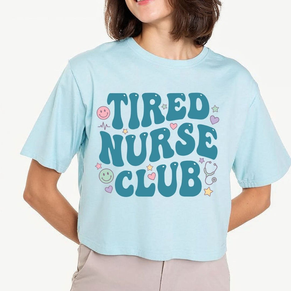 Light blue t-shirt with 'Tired Nurse Club' text and graphics worn by a person.