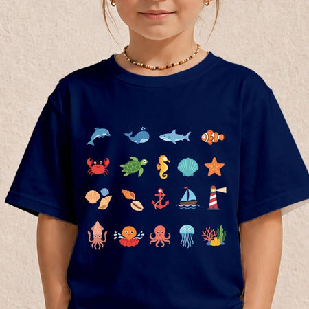 A child wearing a navy blue short-sleeve t-shirt with a colorful graphic print of various sea creatures, including a dolphin, whale, shark, clownfish, crab, turtle, seahorse, shell, starfish, anchor, sailboat, octopus, and coral, displayed against a textured beige wall.