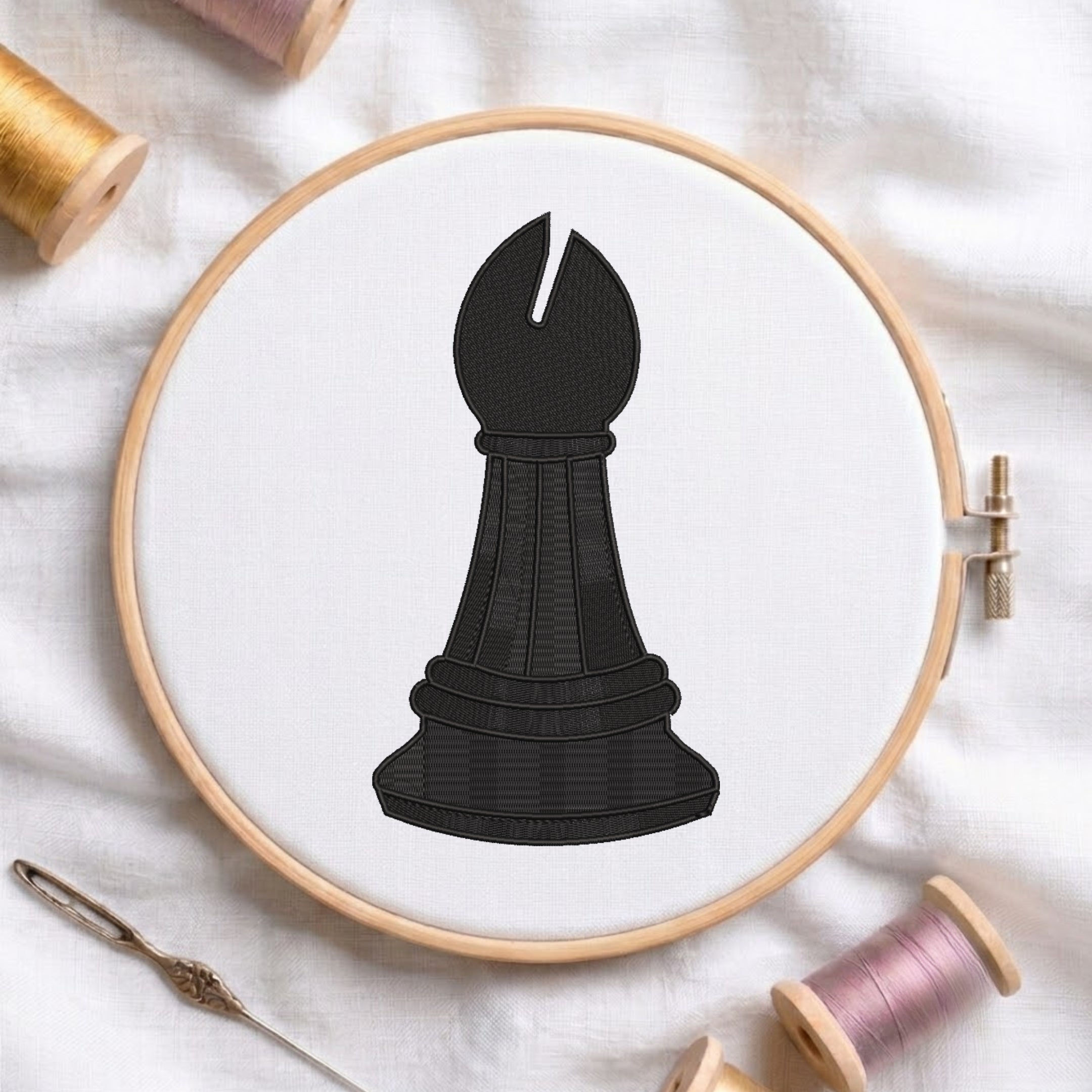 A black chess piece embroidery design displayed inside a wooden embroidery hoop on white fabric, surrounded by spools of thread and a needle.