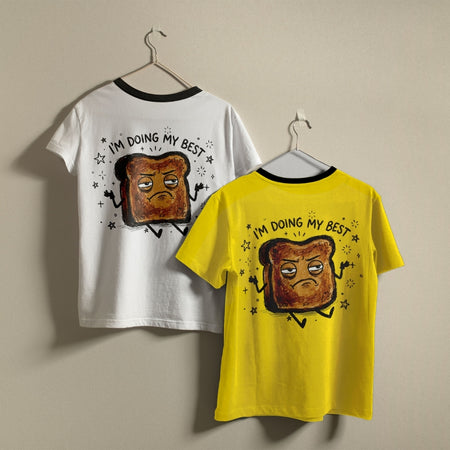 White and yellow t-shirts hanging on a wall, both displaying the humorous burnt toast graphic and quote printed on the back.