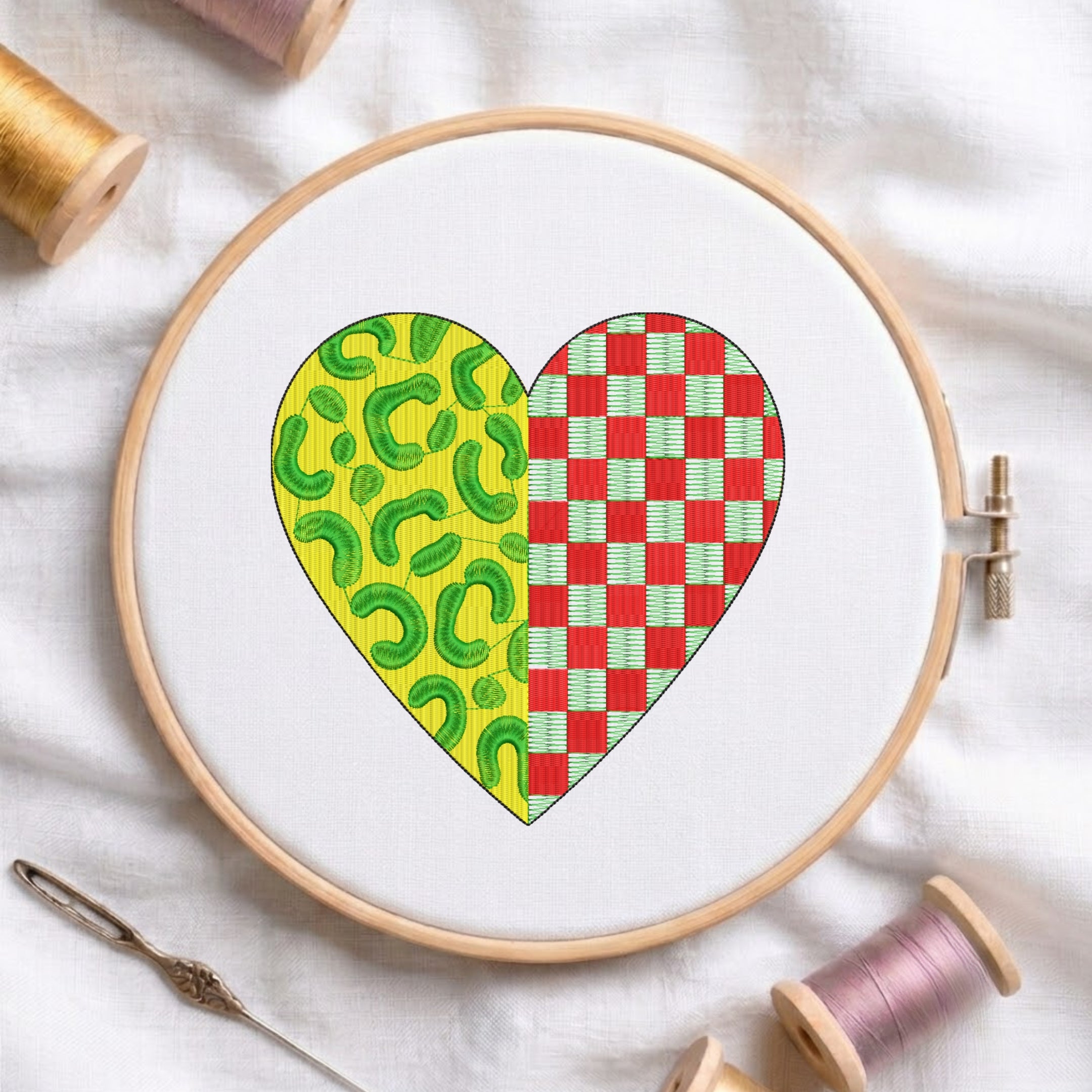 Split heart machine embroidery design featuring green leopard print on yellow and red checkered pattern, displayed inside a wooden embroidery hoop with thread spools.