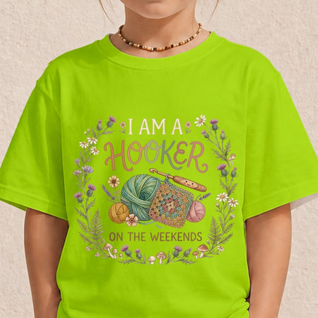 A child wearing a bright lime green t-shirt with a colorful graphic that reads 'I AM A HOOKER ON THE WEEKENDS' surrounded by yarn, crochet hooks, flowers, and mushrooms.