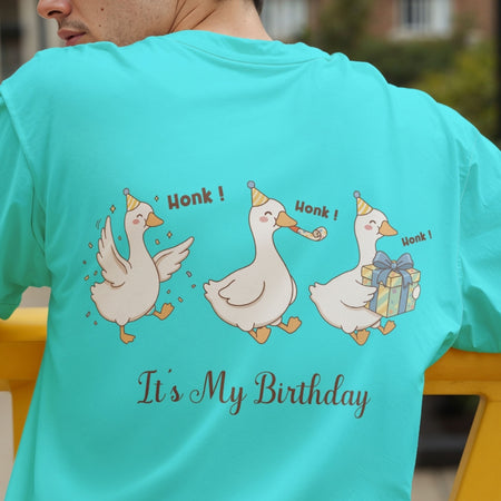 Back view of a person wearing a bright turquoise t-shirt showcasing a funny graphic of three partying geese wearing party hats, holding a present and a party blower, with the text "Honk! Honk! Honk! It's My Birthday".