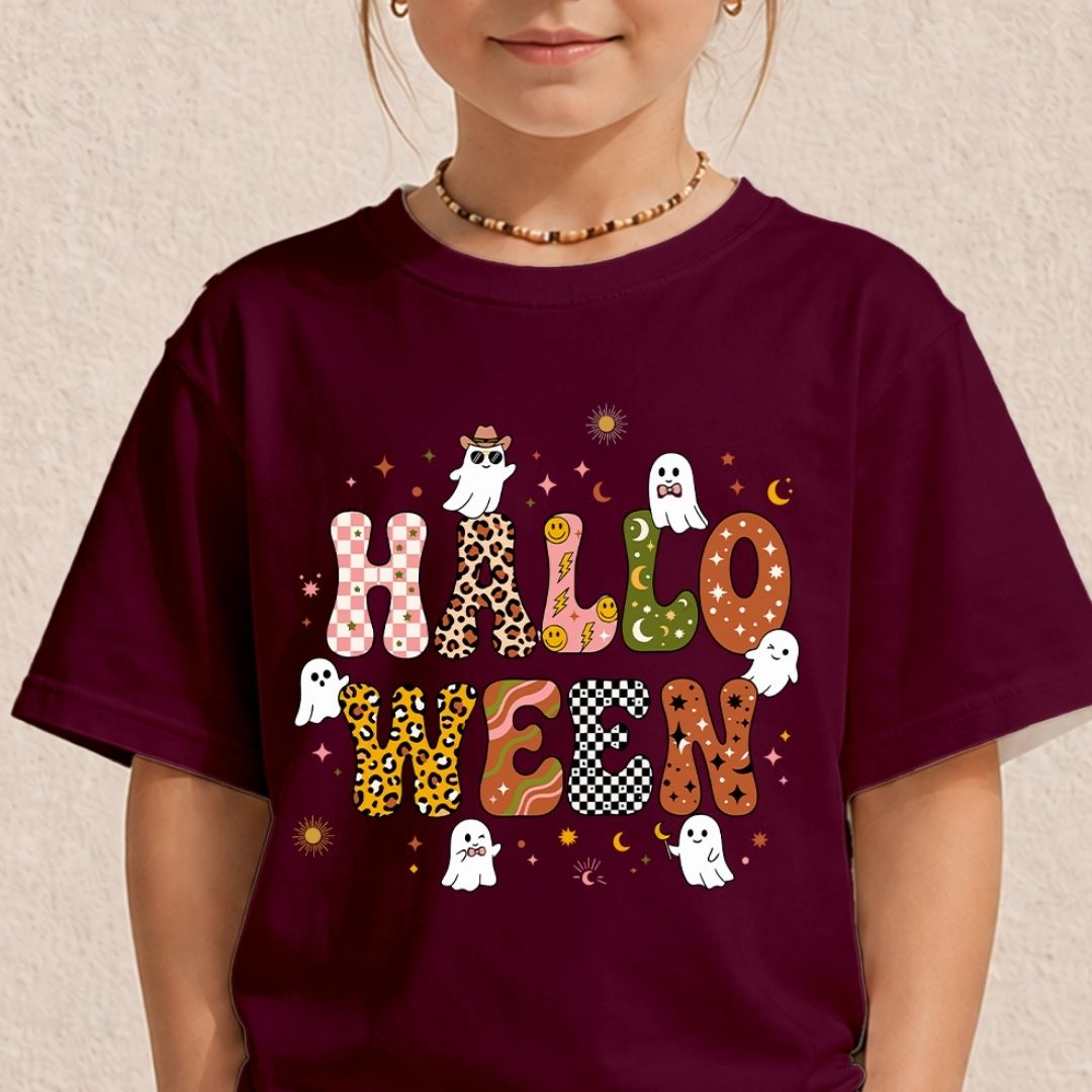A child wearing a dark burgundy t-shirt with a colorful 'HALLOWEEN' graphic featuring patterned letters, ghosts, and stars, set against a textured beige wall.