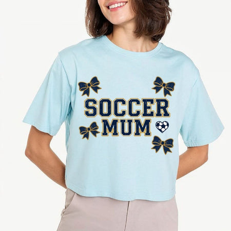 Light blue t-shirt with 'Soccer Mum' text and bow graphics worn by a person.