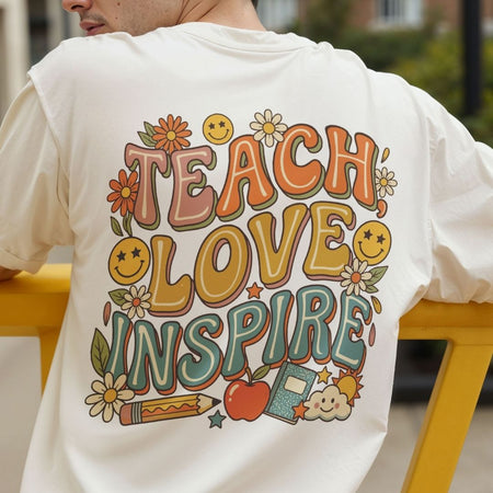 Back view of a person wearing a cream-colored t-shirt showcasing a retro, 70s-style "TEACH LOVE INSPIRE" graphic with smiley faces, daisies, an apple, and a pencil.