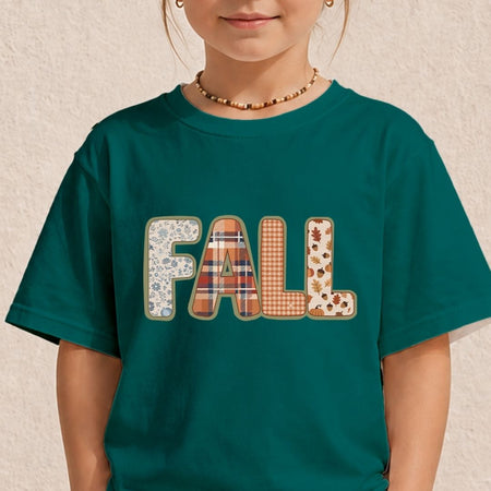 A child wearing a dark teal green t-shirt with the word 'FALL' printed across the chest in a patchwork pattern of plaid, floral, and autumn leaf designs, set against a textured beige wall.