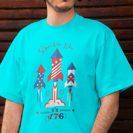Close up of a man wearing a bright turquoise blue t-shirt displaying the red, white, and blue firework rocket digital design on the front.