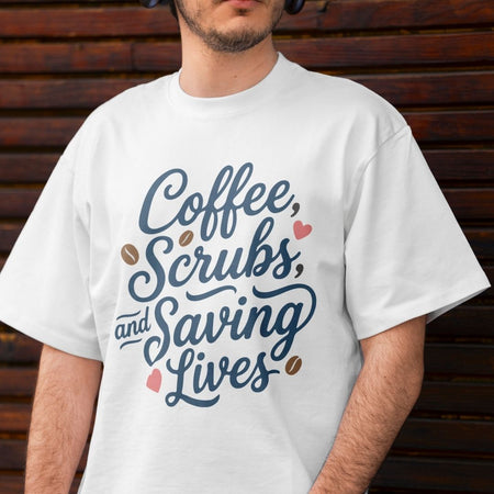 A man wearing a white crewneck t-shirt with a graphic that reads 'Coffee, Scrubs, and Saving Lives' in blue script, decorated with brown coffee beans and pink hearts, set against a dark wooden background.