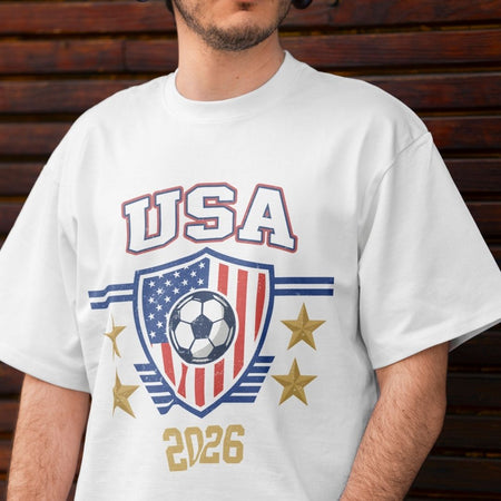 Close-up of a person wearing a white t-shirt featuring a retro USA 2026 soccer graphic with an American flag shield, a soccer ball, and gold stars