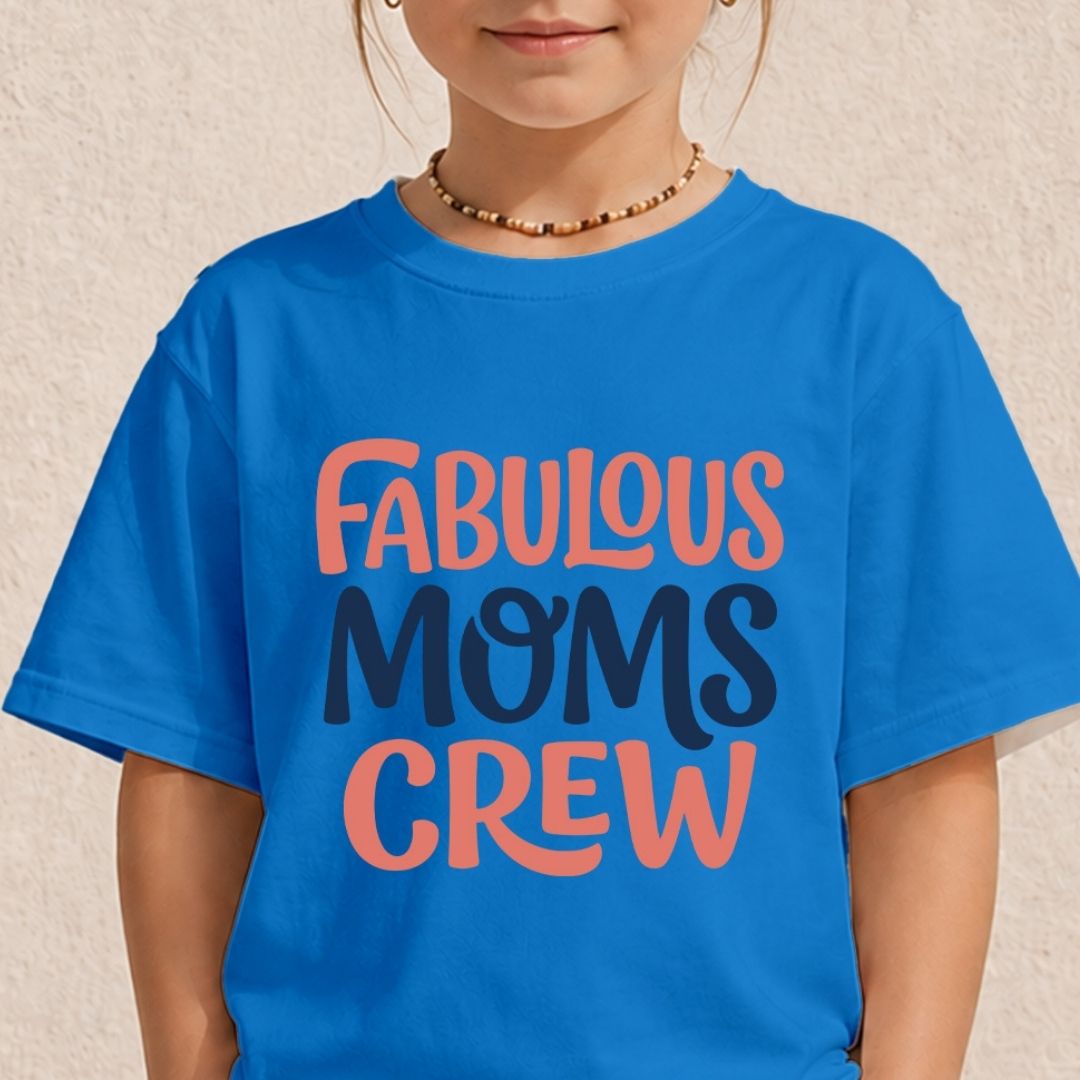 A child wearing a bright blue graphic T-shirt with the words 'FABULOUS MOMS CREW' printed in coral and dark navy lettering, against a light textured wall.