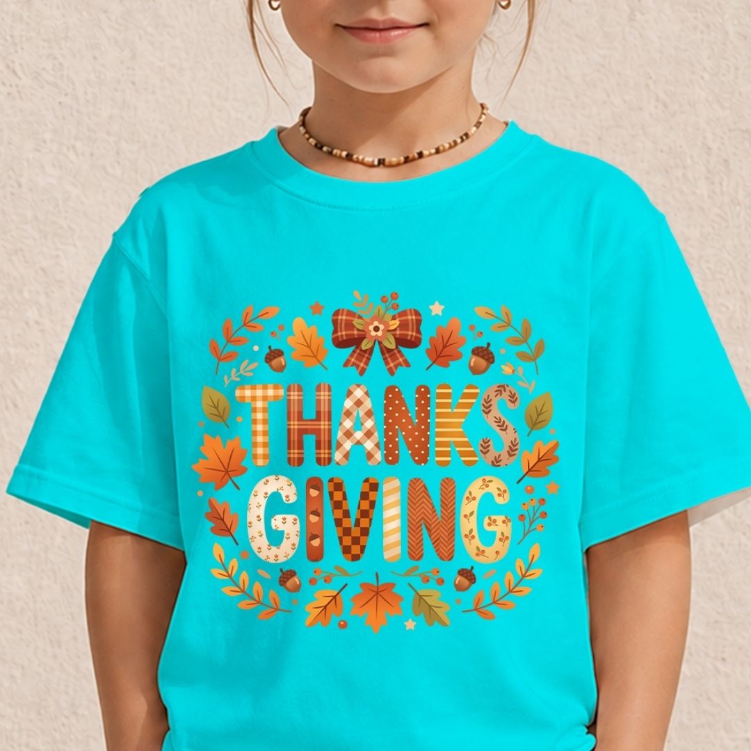 A child wearing a bright turquoise short-sleeve T-shirt with a large autumn-themed 'THANKS GIVING' graphic on the front, featuring fall leaves, acorns, and a bow.