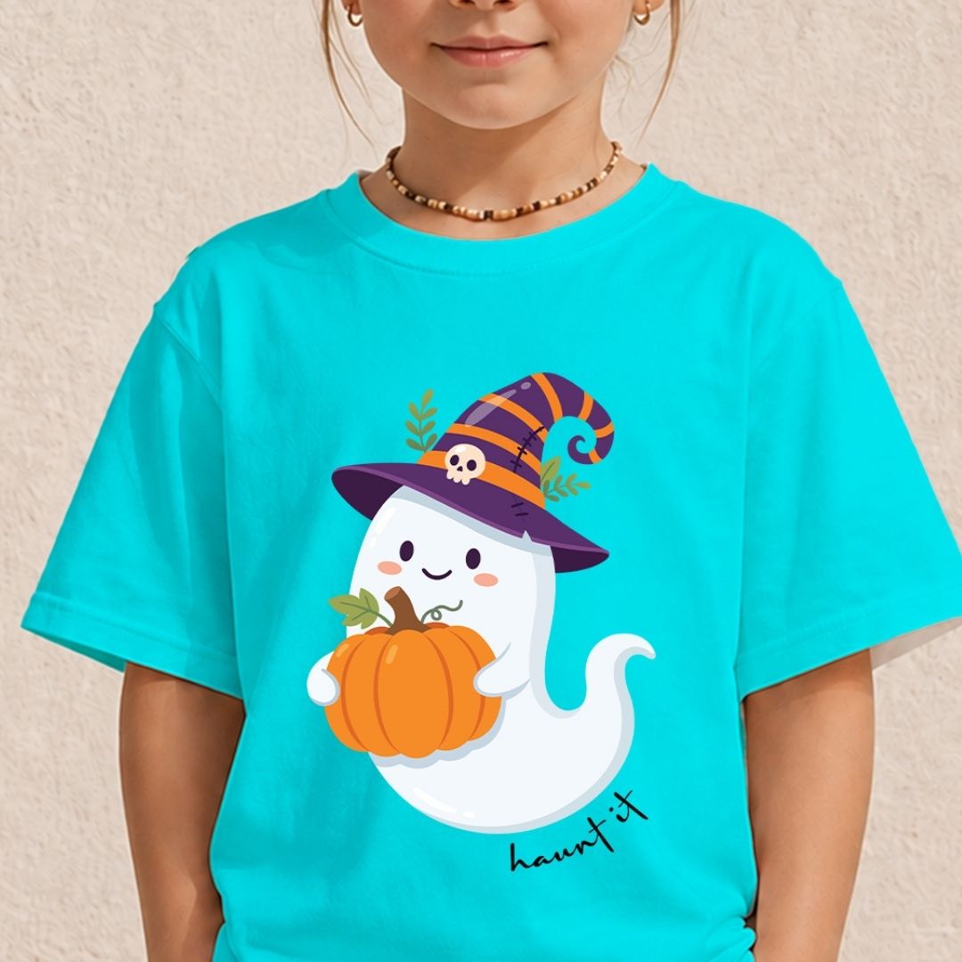 A child wearing a bright turquoise short-sleeve T-shirt with a cute cartoon ghost wearing a purple witch hat and holding an orange pumpkin on the front. The child is shown from the shoulders down against a light beige textured wall.