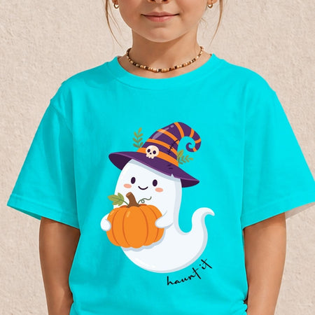 A child wearing a bright turquoise short-sleeve T-shirt with a cute cartoon ghost wearing a purple witch hat and holding an orange pumpkin on the front. The child is shown from the shoulders down against a light beige textured wall.