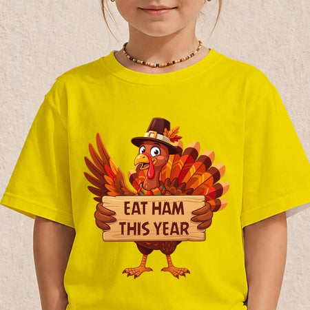 A child wearing a bright yellow t-shirt with a cartoon turkey graphic holding a sign that reads 'EAT HAM THIS YEAR'.