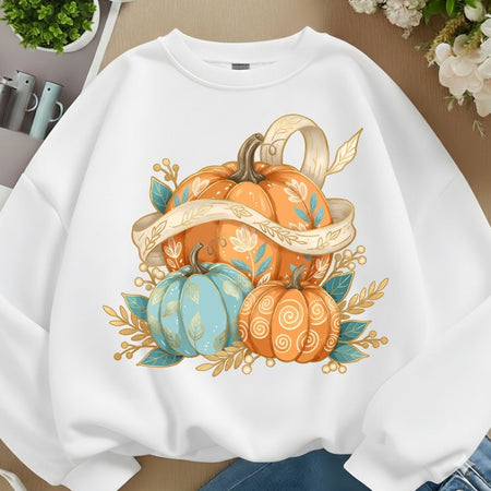 A white crewneck sweatshirt featuring a colorful autumn graphic of three stylized pumpkins in orange, light blue, and gold-toned leaves and ribbons, shown laid flat on a neutral surface.
