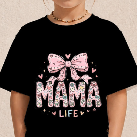 Close-up of a child wearing a black t-shirt printed with a colorful pastel "MAMA LIFE" text illustration featuring a patterned design and a large pink ribbon bow.