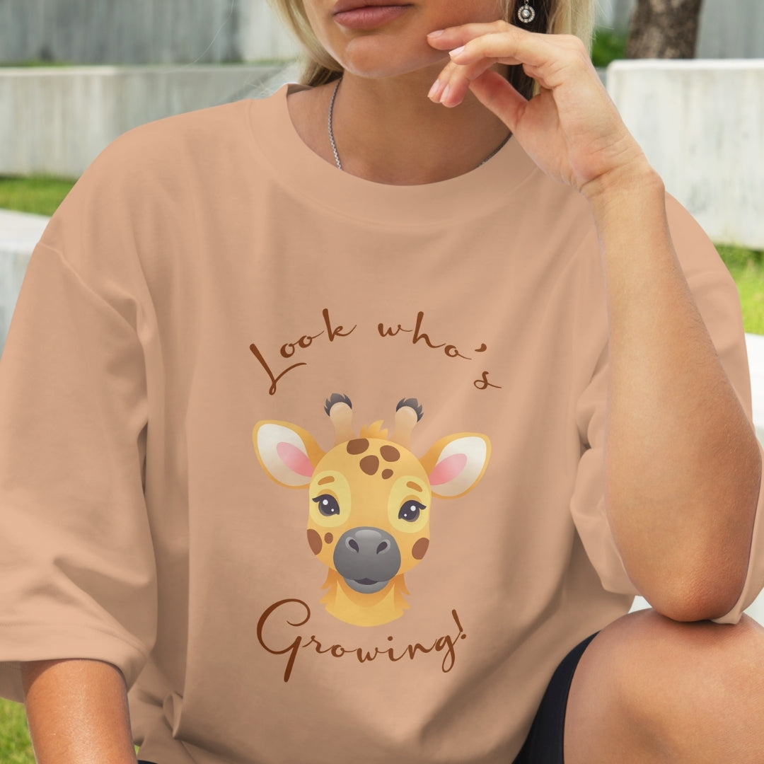 Person wearing a beige t-shirt with a giraffe graphic and text outdoors.