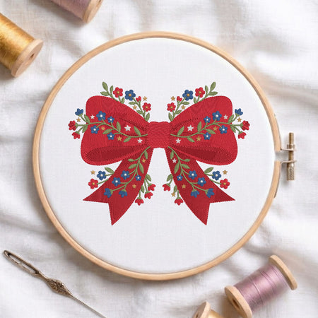 Red ribbon bow embroidery design detailed with blue and red floral embroidery stitches inside a wooden hoop.