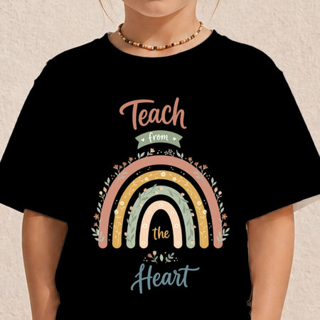 A person wearing a black short-sleeve T-shirt with a colorful rainbow graphic and the words 'Teach from the Heart' printed on the front, against a light textured wall.